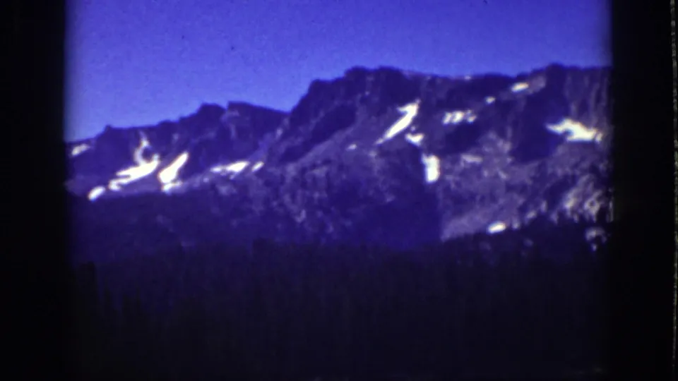 Vintage 8mm Lake Tahoe frame showing rocky alpine slopes with scattered snow above dark evergreens.