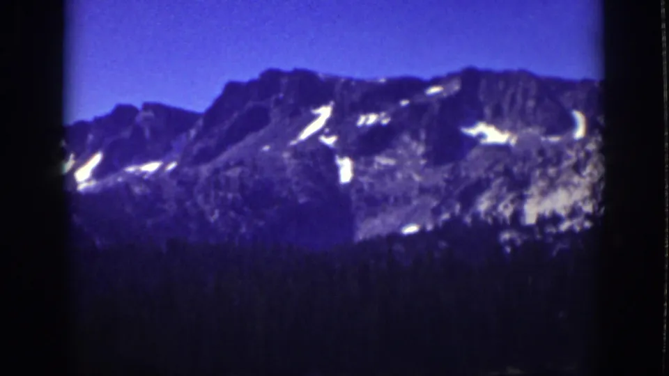 1939 Lake Tahoe landscape frame with snow-marked mountain ridge, blue sky, and dark conifer forest foreground.