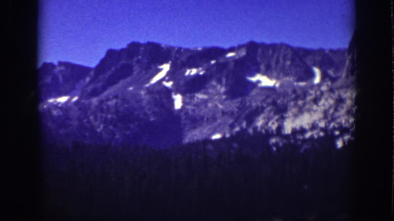 1939 Lake Tahoe 8mm frame showing a rocky Sierra Nevada ridge, small snow patches, blue sky, and dark trees below.