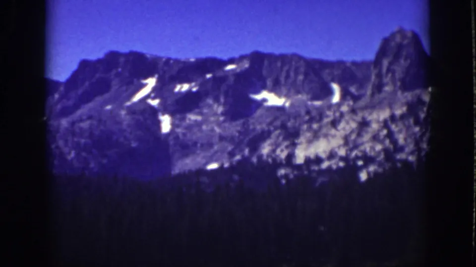 1939 Lake Tahoe 8mm view of a rugged mountain ridge with scattered snow, dark tree line, and blue-purple film color.