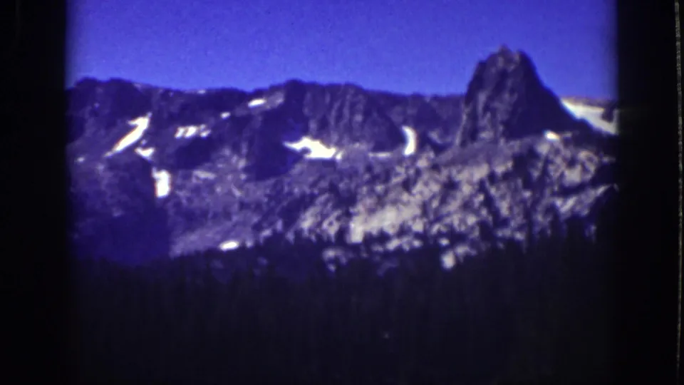1939 Lake Tahoe 8mm frame with a prominent rock outcrop, snow patches, blue sky, and forested lower slope.