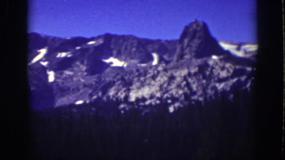 1939 Lake Tahoe 8mm view of a snow-patched mountain ridge and dark forest foreground under a blue sky.