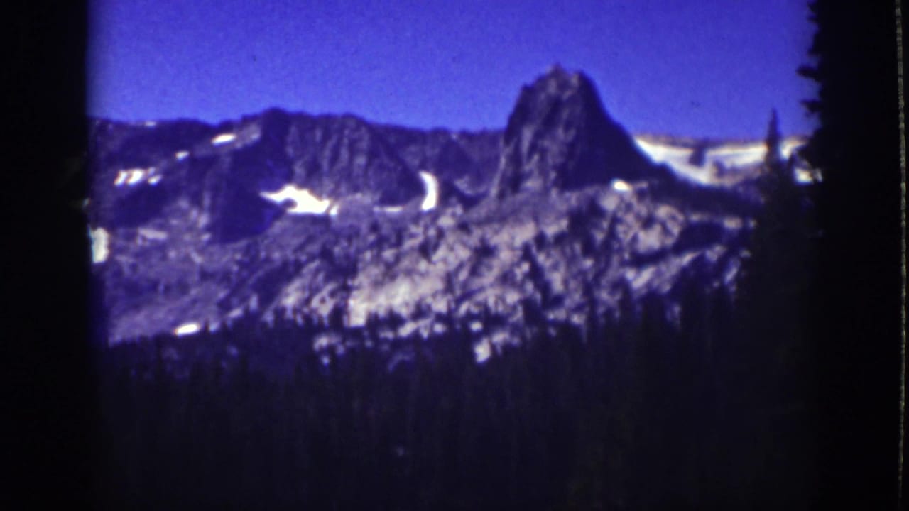 Distant mountain ridge with snow patches framed by dark trees and film-edge shadows.
