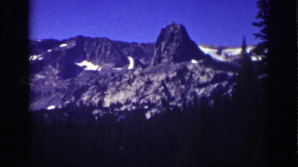Lake Tahoe 8mm view of a rocky mountain range, bright snow patches, and a dark pine foreground beneath blue sky.