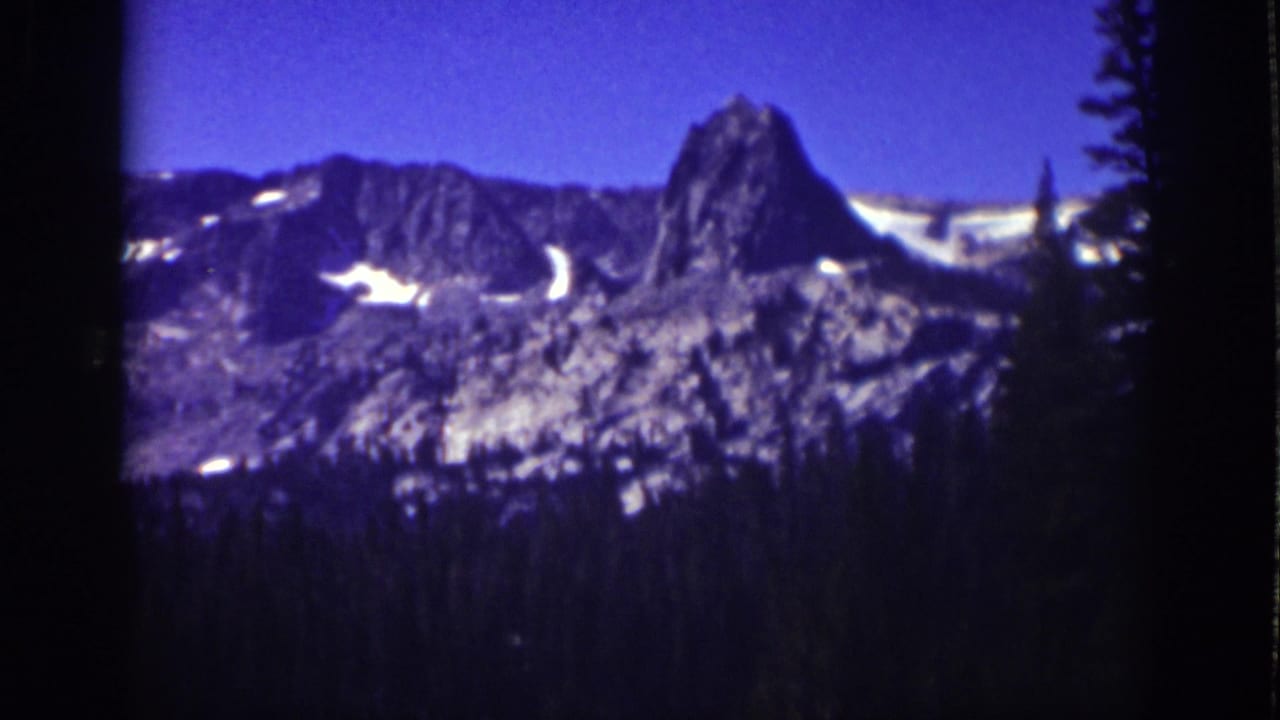 1939 Lake Tahoe home-movie frame showing a rugged snow-patched mountain ridge beyond a dark evergreen foreground.