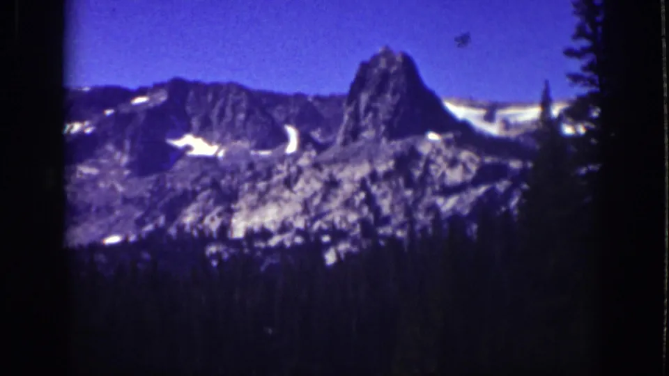 Lake Tahoe 8mm frame from 1939 showing a still mountain vista with snow on the rocks and evergreen silhouettes nearby.