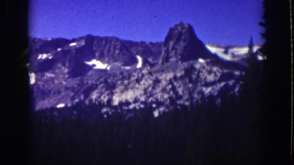 1939 Lake Tahoe 8mm view of a jagged mountain formation with snow patches and dark forest in the foreground.