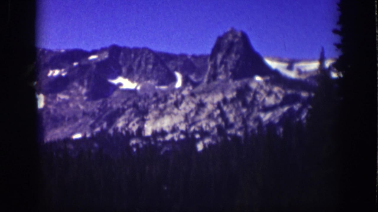 Distant rocky peak and ridgeline with snow patches above a shadowed tree line.