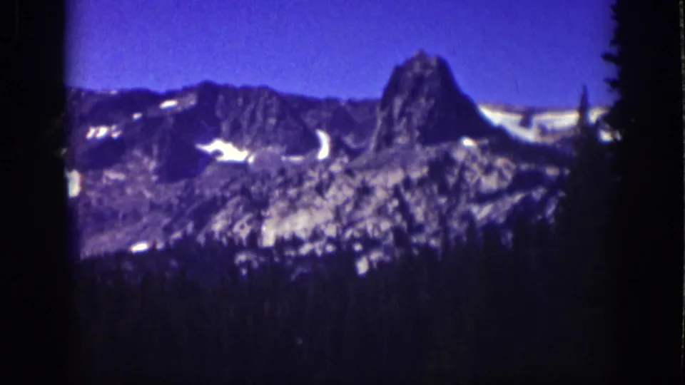 Lake Tahoe mountain landscape on 8mm film, showing a rugged peak, snow-streaked slopes, and dark evergreens.