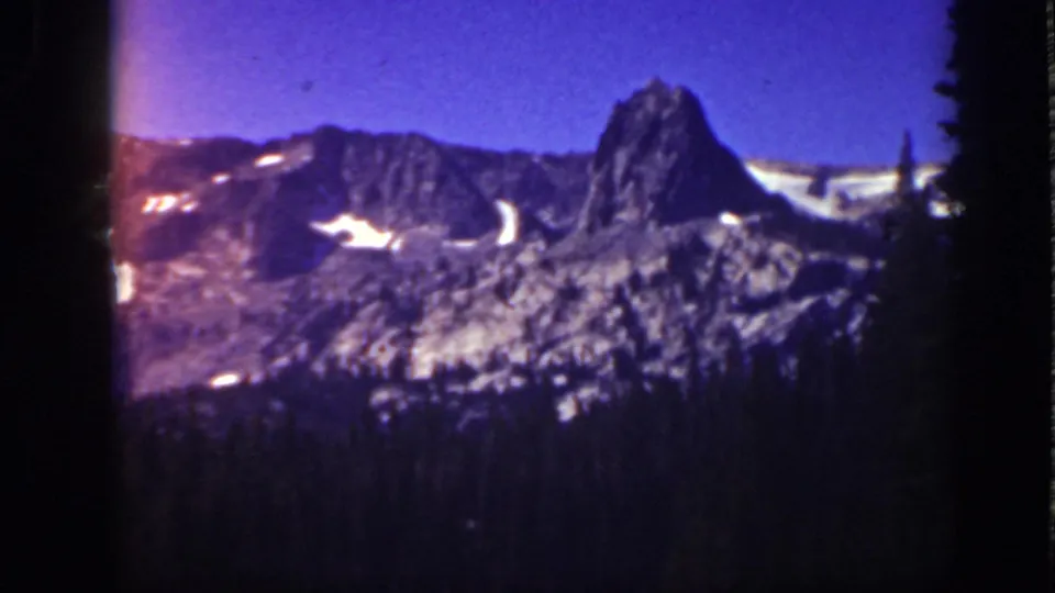 1939 Lake Tahoe 8mm frame of a rugged snow-patched mountain, with visible color flare and dark forest below.
