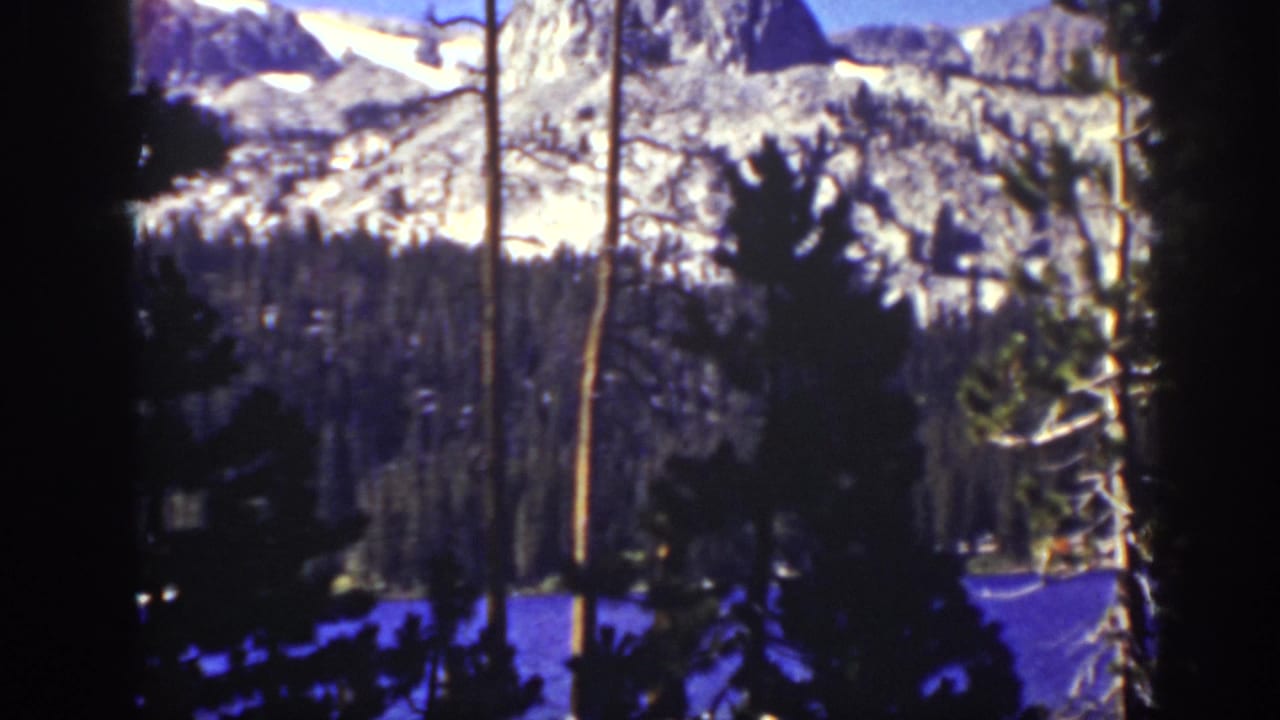 1939 Lake Tahoe-area 8mm frame showing a distant snow-streaked mountain ridge behind pine silhouettes and bare trunks.