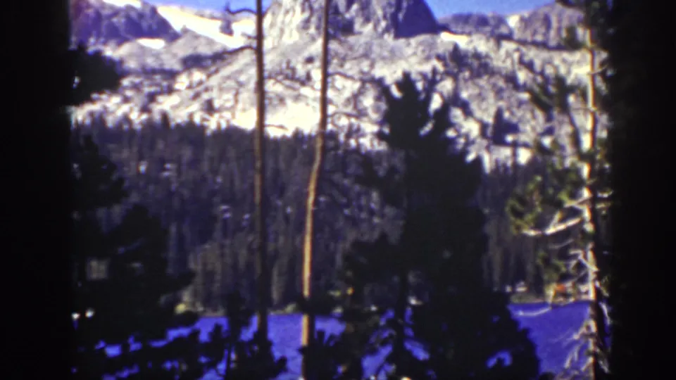1939 Lake Tahoe-area 8mm frame showing a distant snow-streaked mountain ridge behind pine silhouettes and bare trunks.