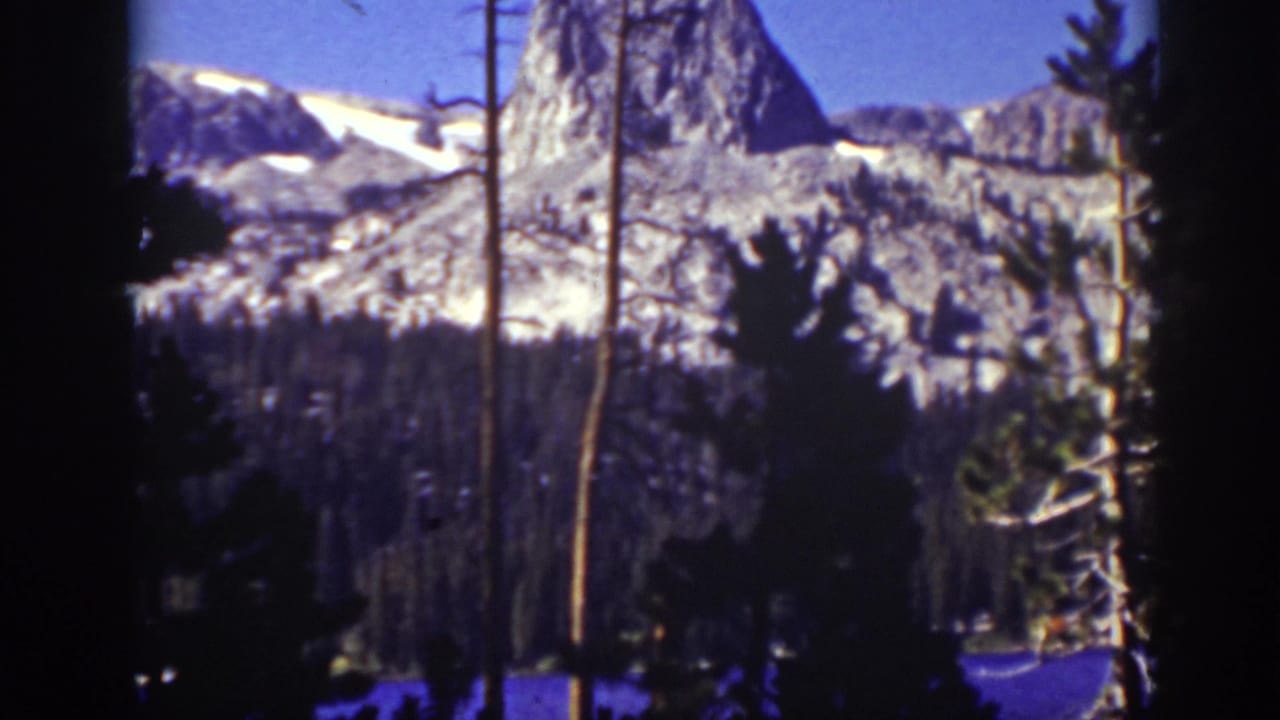 Rocky mountain peak and snow patches framed by dark trees.