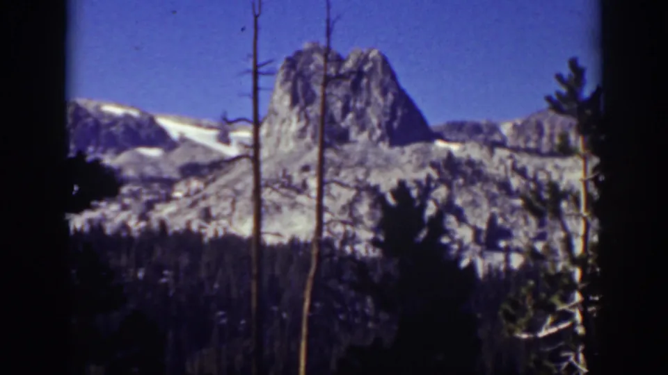 1939 Lake Tahoe-area landscape frame with a distant snow-marked peak, dark pine foreground, and visible 8mm scan borders.