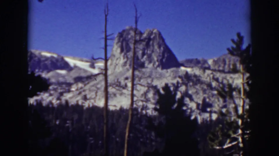 1939 Lake Tahoe 8mm frame showing a rocky Sierra Nevada peak above dark trees and bare trunks beneath a deep blue sky.