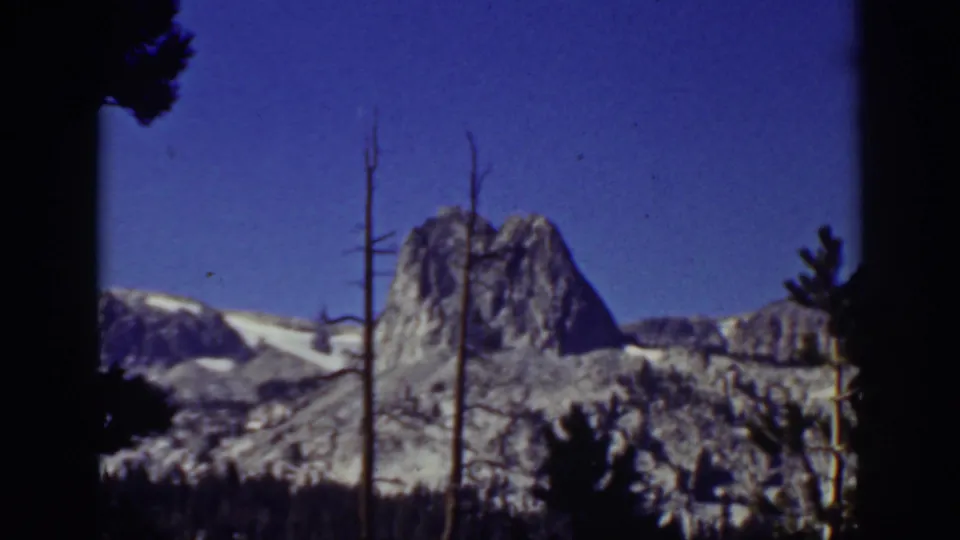 Lake Tahoe 1939 8mm frame showing a snow-dusted rocky summit and silhouetted trees under a clear blue sky.