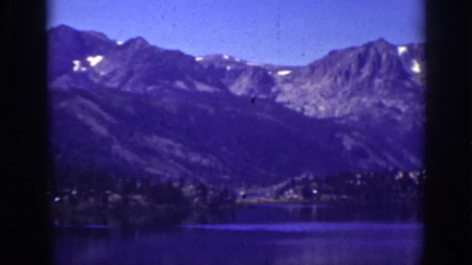 Vintage 8mm Lake Tahoe frame showing blue-toned mountains, snow patches, a forested shoreline, and still lake water.