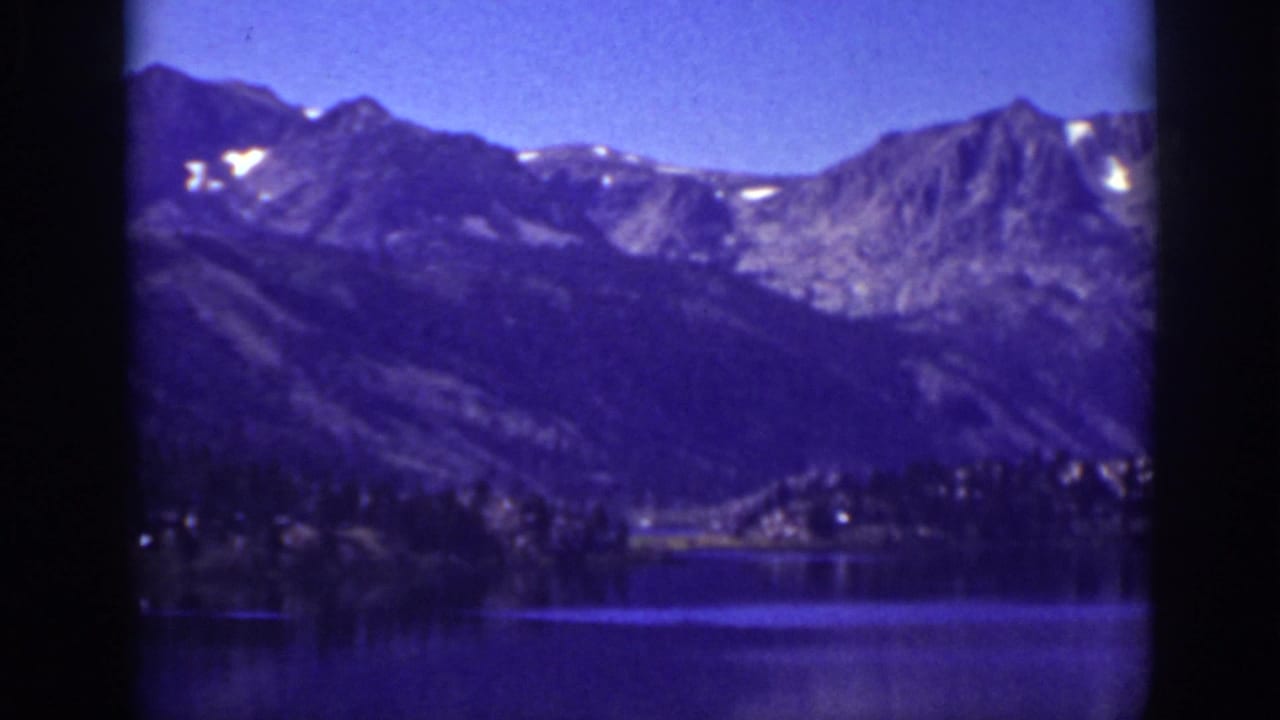 1939 Lake Tahoe home-movie frame showing blue lake water, wooded shoreline, and distant mountain ridges with small snow patches.