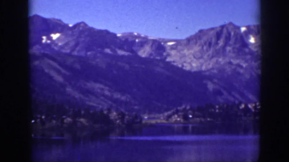 1939 Lake Tahoe frame with soft 8mm texture, showing water in the foreground and high mountain ridges beyond the shoreline.