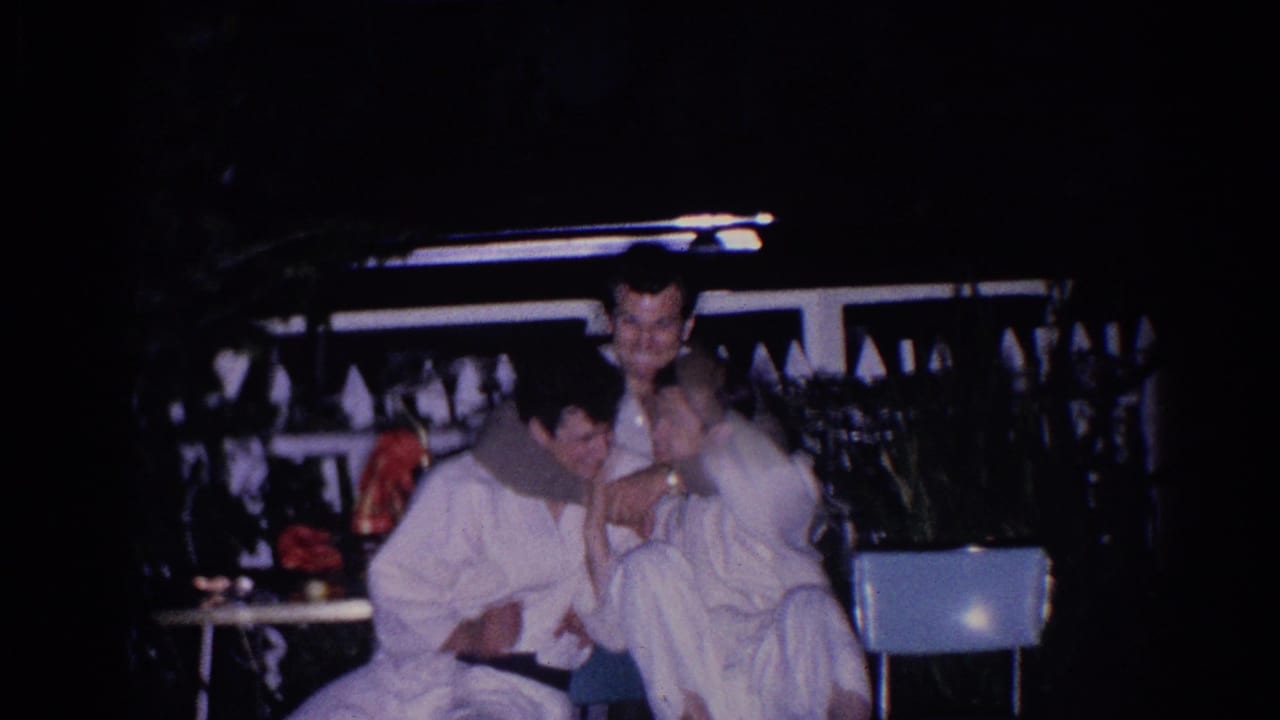 A seated man in a white uniform smiles while another man stands behind him near a chair.