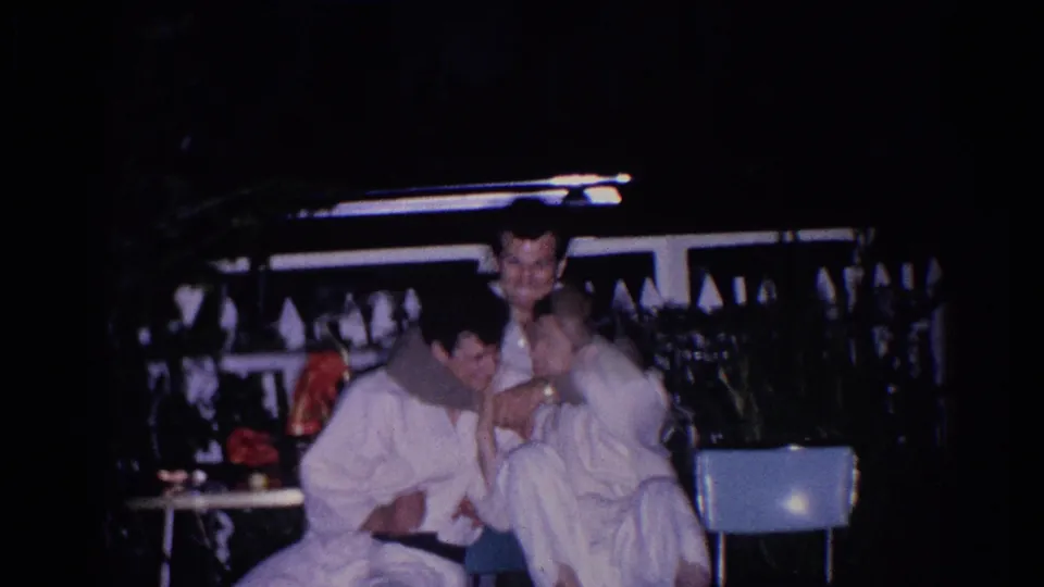 In the El Monte 1966 scene, a seated man in a white uniform smiles as another uniformed man stands nearby under artificial light.