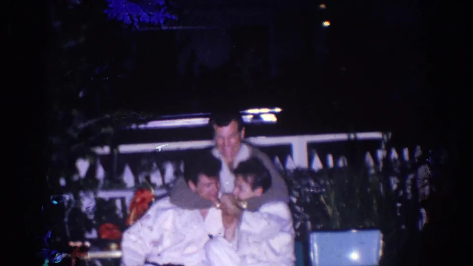 Three men in white uniforms gather closely in the El Monte night scene, suggesting informal pre-match interaction or camaraderie.