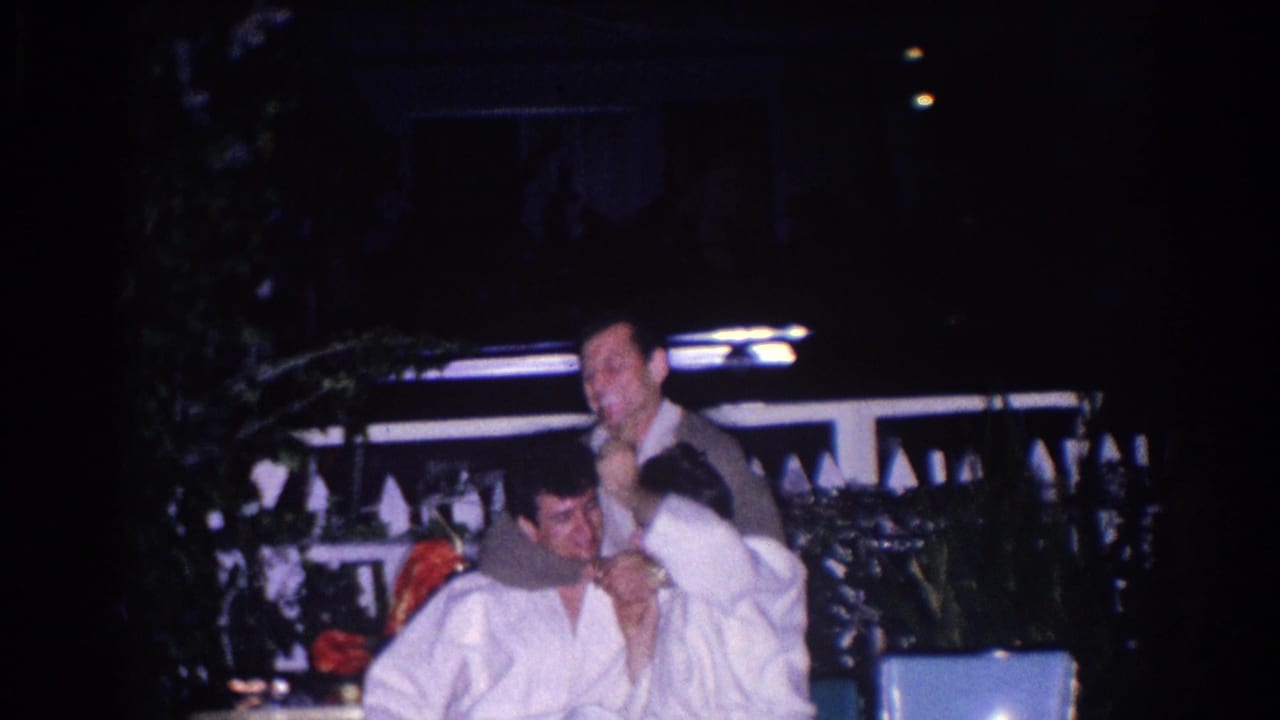 Two young men in white uniforms sit on a dark patio while another man stands behind them.
