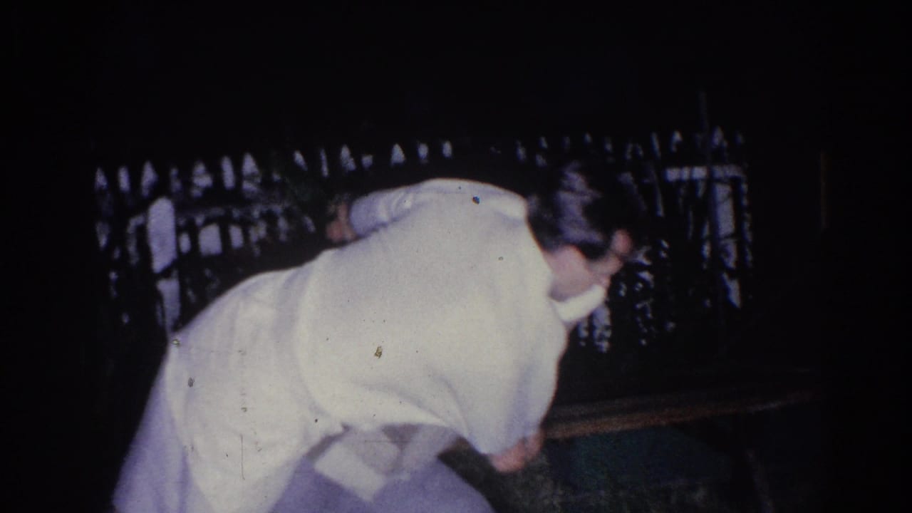 Adult man in light clothing bends forward at night near a white fence.