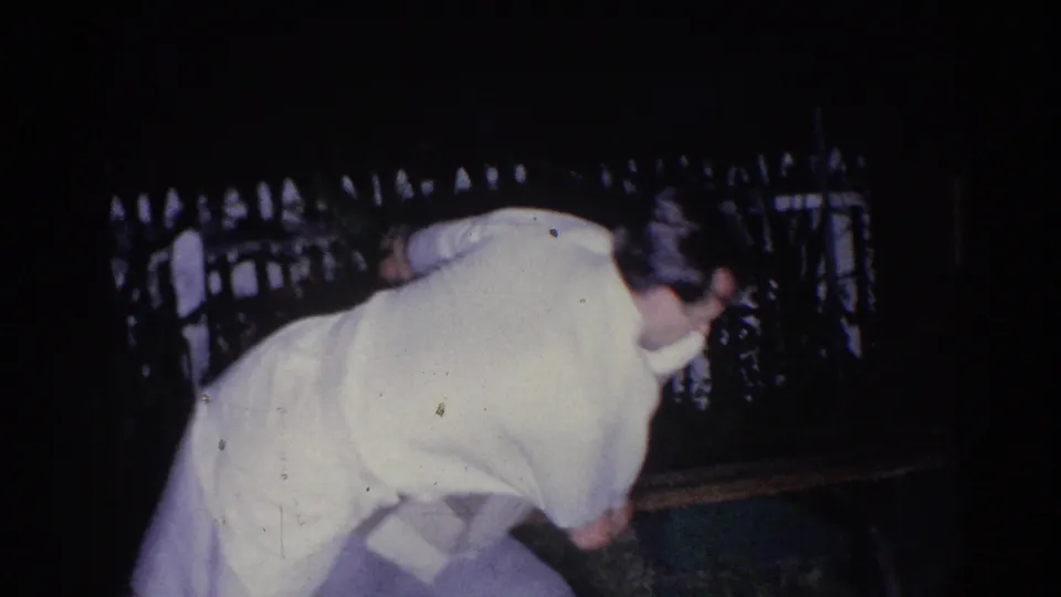 In the 1966 El Monte home-movie clip, an adult man in light clothing bends during nighttime karate practice near a white fence.