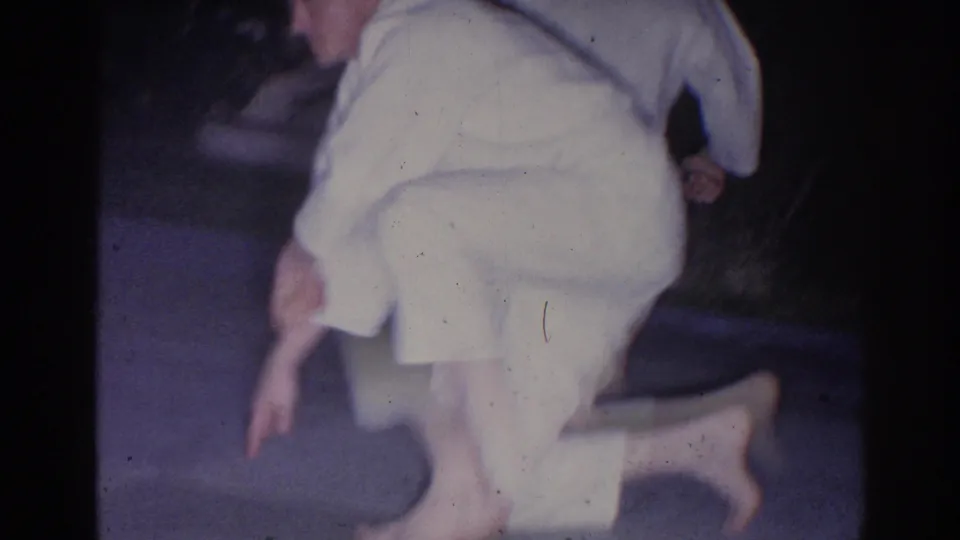 An adult man in light clothing crouches or kneels on pavement in the nighttime El Monte backyard karate practice footage.