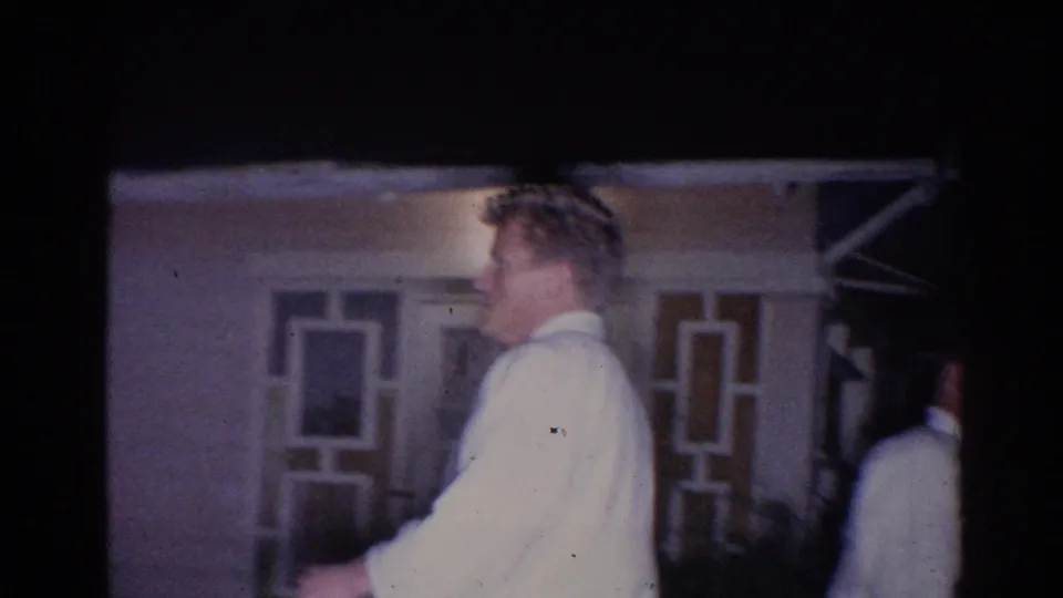 In 1966 El Monte footage, a man in a white gi moves near a building entrance under dim nighttime light.