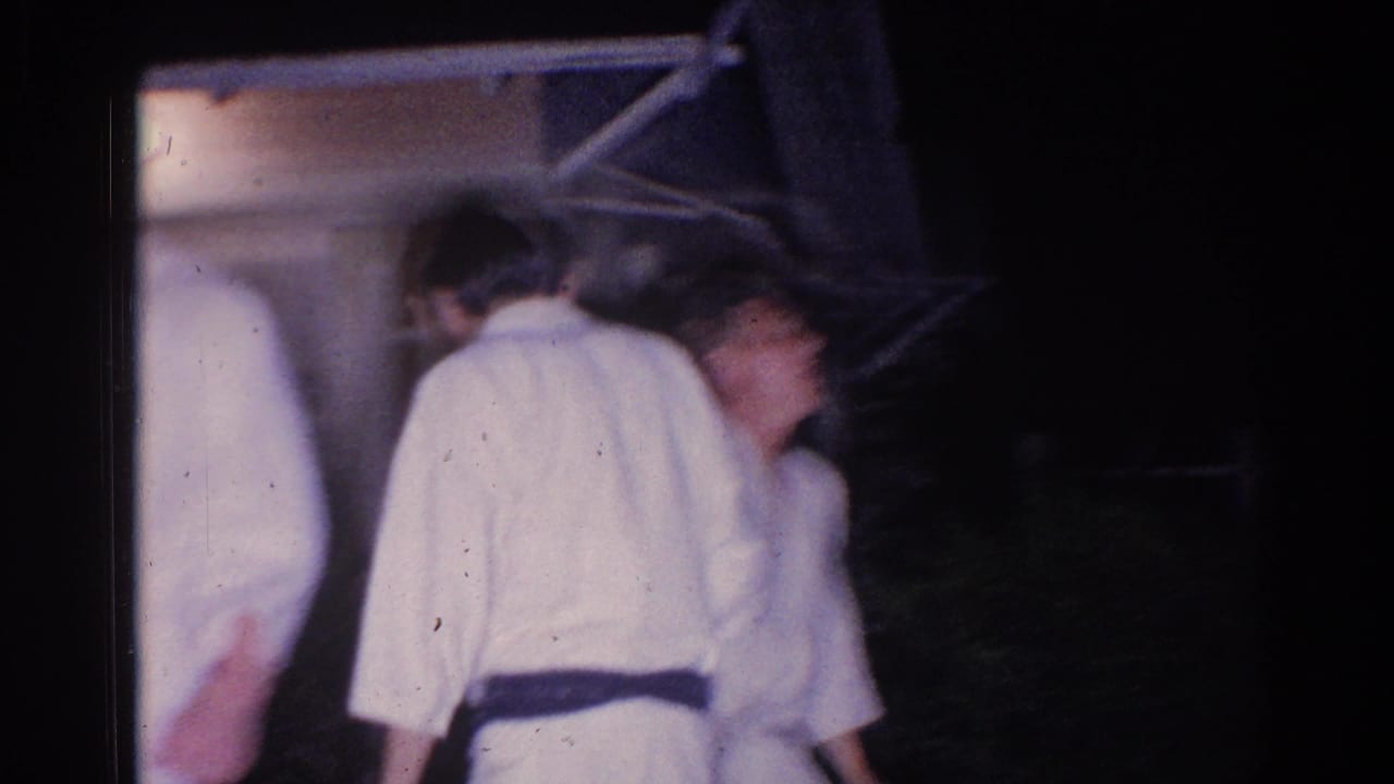 Several people in white karate uniforms stand close together outside at night.