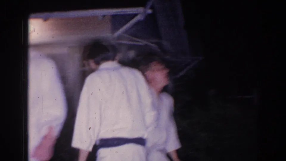 Men in white gi gather near an exterior structure during the nighttime El Monte martial arts scene.