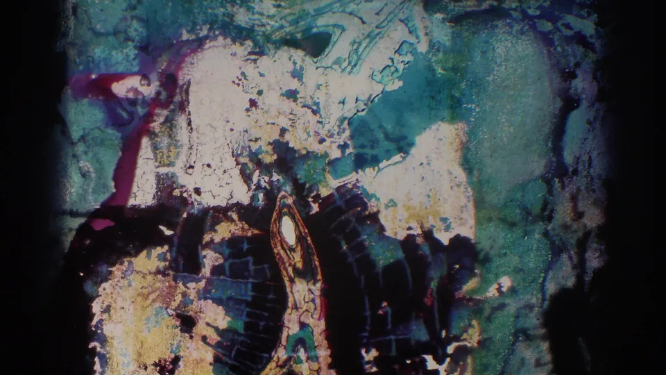 A damaged or transitional 8mm frame shows mottled green, white, and dark color patterns with no clear figures.