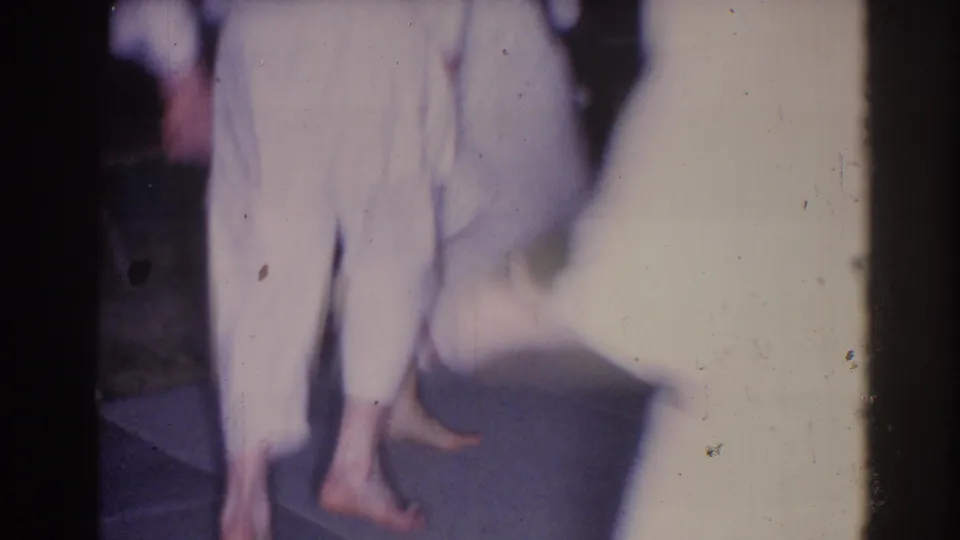 Blurred 1966 8mm frame from El Monte showing people in white clothing moving through a dark outdoor gathering.