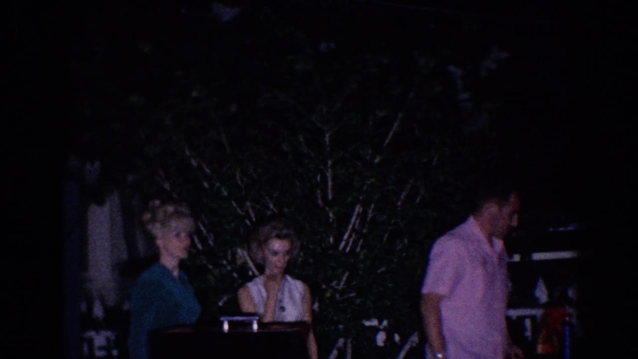 Two women and a man stand outdoors at night near a dark piano-like object.
