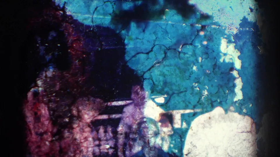 Low-light 8mm frame from the El Monte clip with partial adult figures, heavy color shift, and visible film wear.