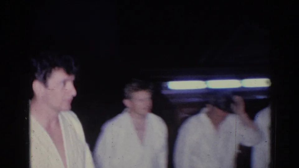 El Monte, 1966 home-movie frame with several men in white robes or light garments standing under artificial light.