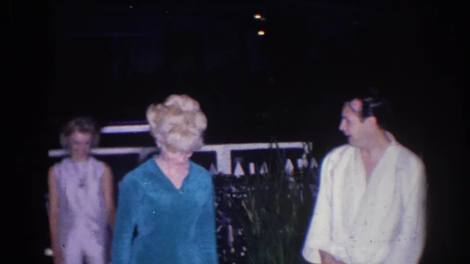 Two women and a man are framed together at the 1966 nighttime gathering, with soft focus and handheld 8mm texture.