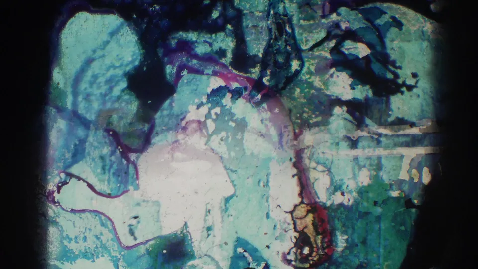Damaged or transitional 8mm frame with blue-green chemical-looking patterns and irregular dark marks.