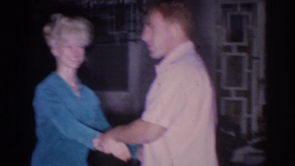 1966 El Monte home-movie frame of two adults smiling and holding hands, possibly dancing, at night.