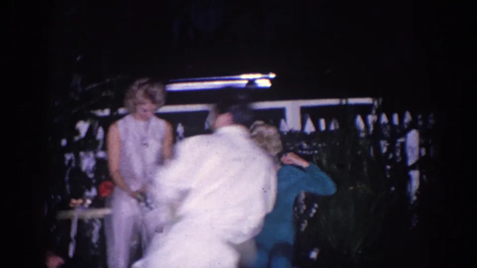 A 1966 El Monte home-movie frame shows adults at night, with a blurred person crossing in front and a woman in white by the railing.