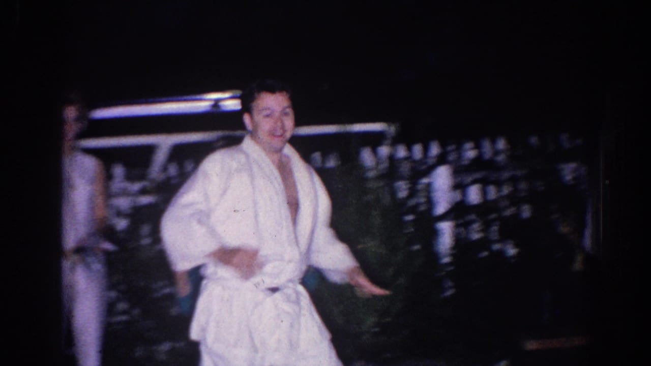 Young man in a white martial arts uniform stands outdoors at night near a fence or railing.