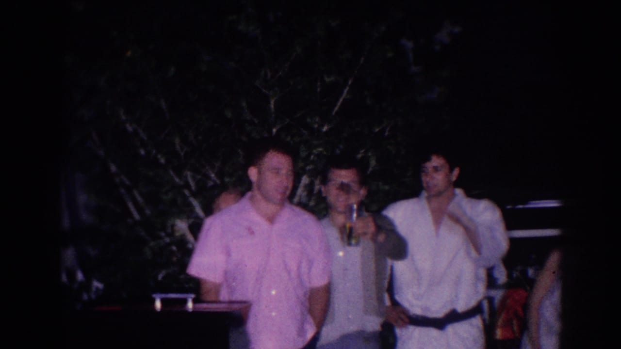 In 1966 El Monte home-movie footage, three adult men stand together at a nighttime backyard gathering, one holding a drink.
