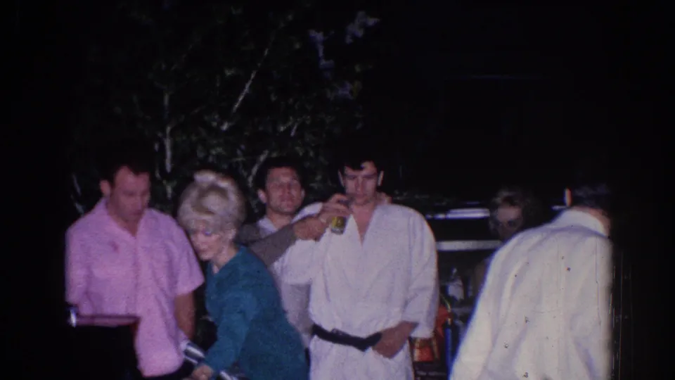 Adults socialize in a dim El Monte backyard scene, with a woman in teal and a man in a white martial-arts uniform visible.