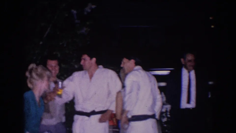 In the supplied 1966 El Monte clip, judo athletes in white gi and nearby adults gather under artificial light during a break.