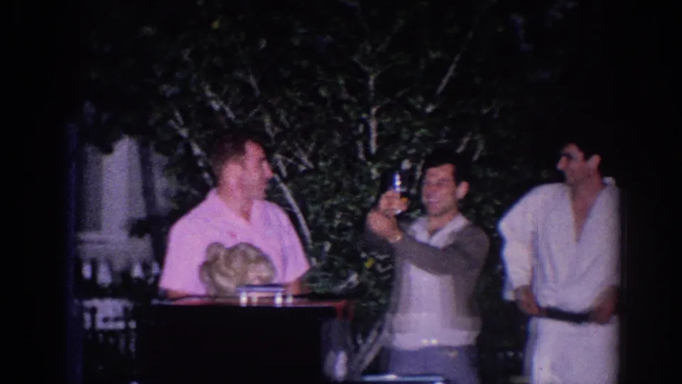 Adults and judo athletes stand together in 1966 El Monte footage, with one person lifting a cup beside a man in a pink shirt.