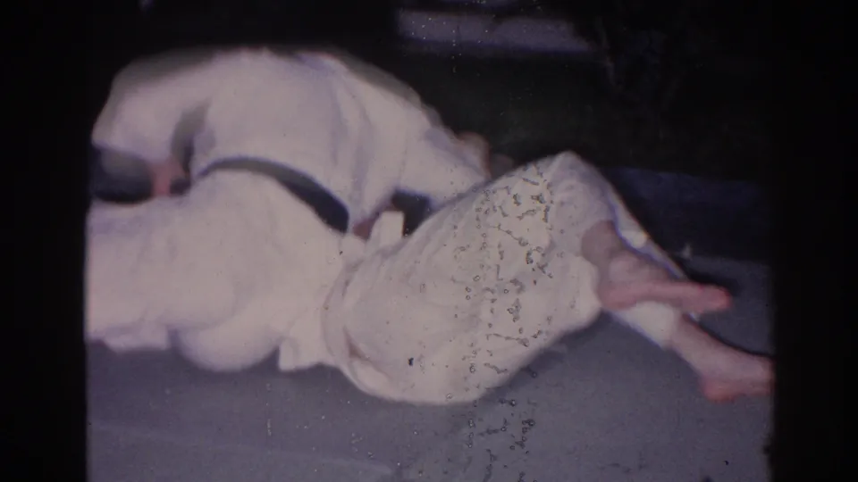 A person in light clothing appears reclined in a dim, soft-focused 1966 El Monte home-movie frame.