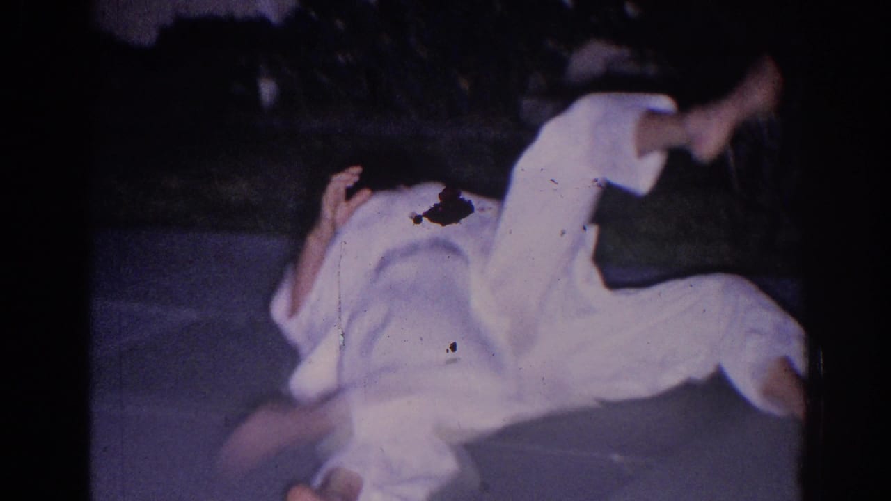 A person in a white gi rolls on the pavement during martial arts practice.