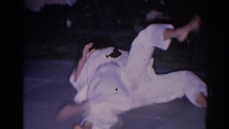 1966 El Monte frame showing a white-gi martial artist mid-roll or takedown on an outdoor paved surface at night.